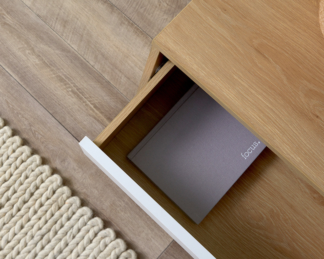 Open drawer of coastal bedside pedestal showing wooden finish and a book inside on a hardwood floor