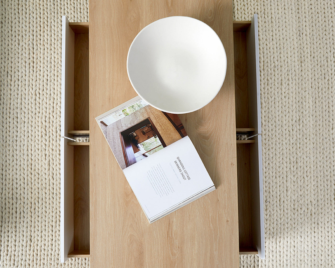 Modern minimalist coffee table by Imperial Homes with light wood finish, white bowl, and open drawers